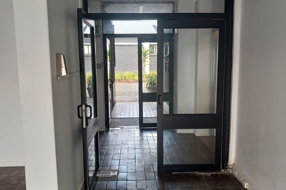 A functional office entrance featuring black aluminium glass doors and tiled flooring, providing direct access to an outdoor paved area.