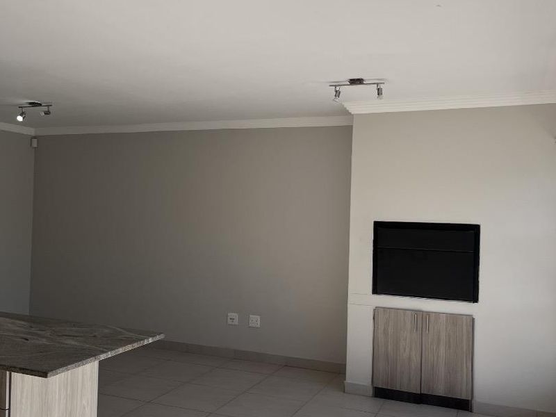 Spacious open-plan living area featuring tiled floors, modern track lighting, and a built-in cabinetry unit with a recessed wall feature.