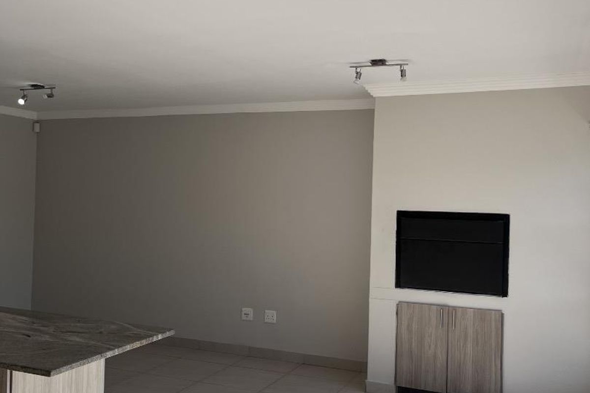 Spacious open-plan living area featuring tiled floors, modern track lighting, and a built-in cabinetry unit with a recessed wall feature.
