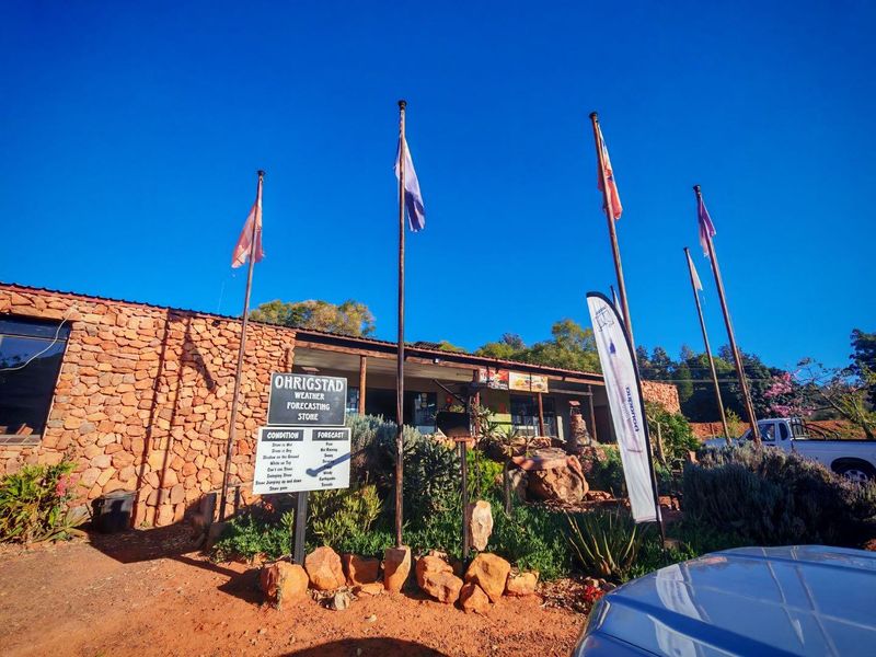 Front elevation of a commercial property featuring rustic stone cladding, multiple flagpoles, and a landscaped garden area.