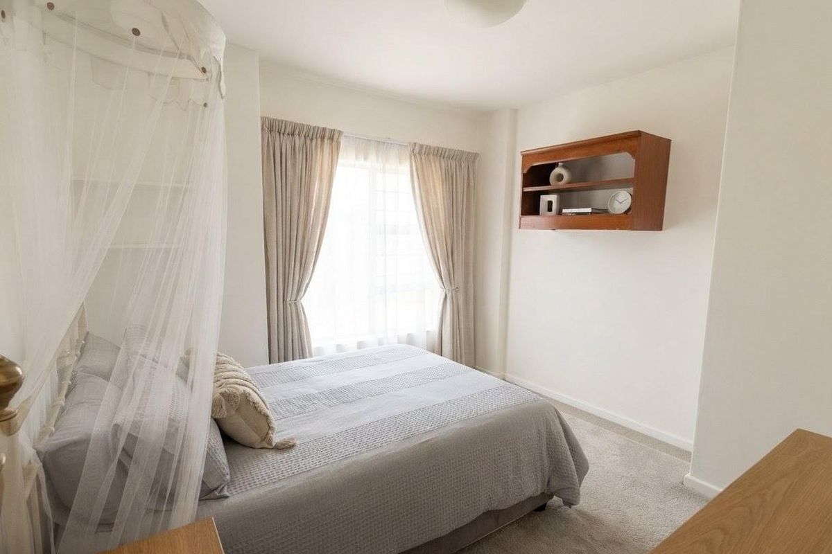 A well-maintained bedroom featuring neutral carpeting, built-in wall shelving, and natural light through a window with curtains.