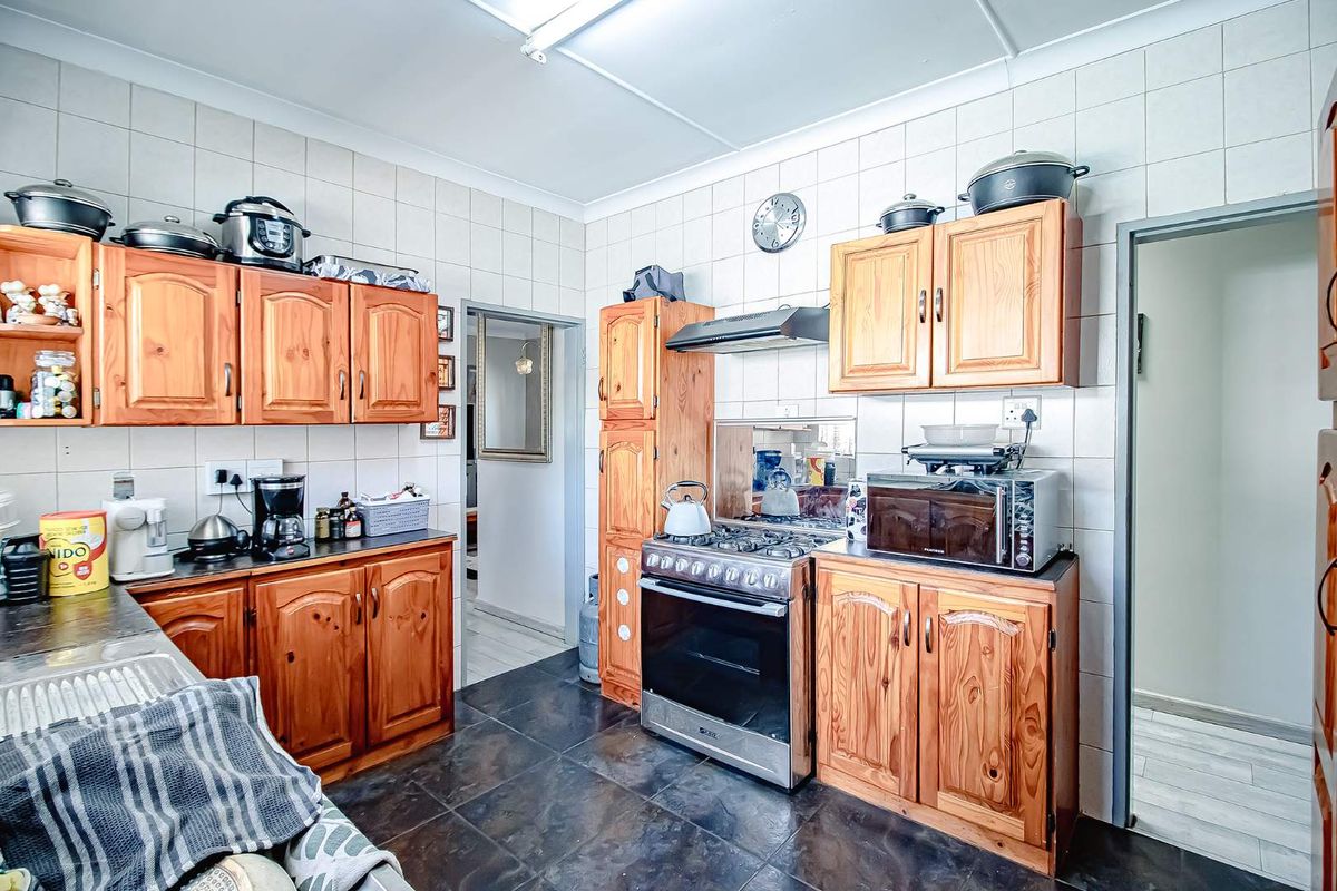 A functional kitchen featuring wooden cabinetry, a stainless steel gas stove with extractor fan, and dark tiled flooring.