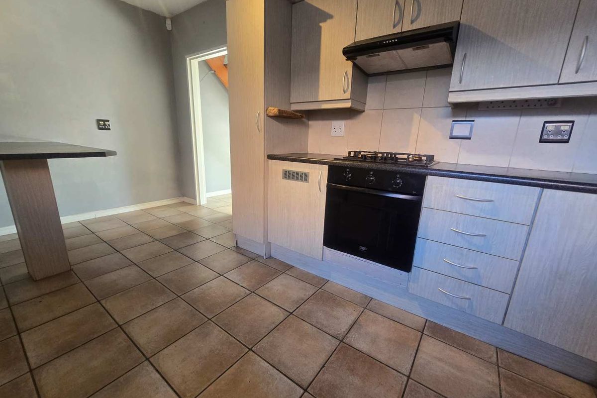 A functional kitchen featuring built-in cabinetry, a gas hob, electric oven, extractor fan, and a breakfast bar, finished with tiled flooring.
