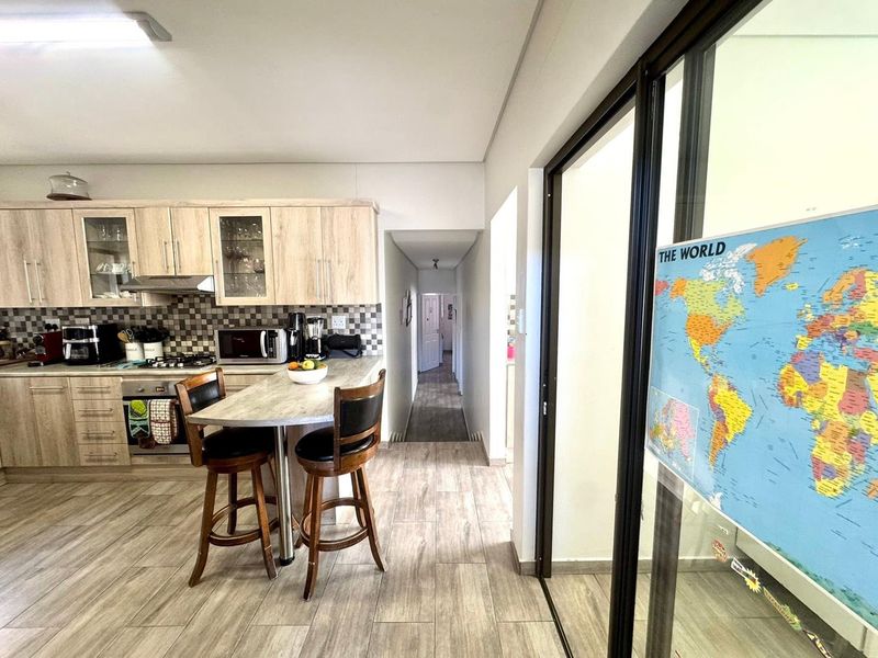 A functional kitchen featuring light wood-toned cabinetry, a tiled backsplash, integrated appliances, and a breakfast bar, leading into a hallway with wood-look flooring.