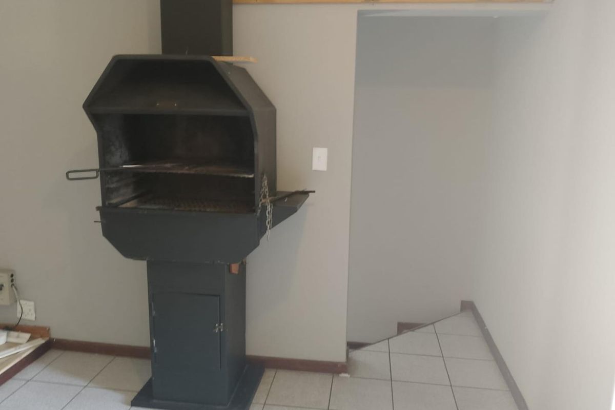 Indoor entertainment area featuring a built-in metal braai fireplace, tiled flooring, and direct access to a staircase.