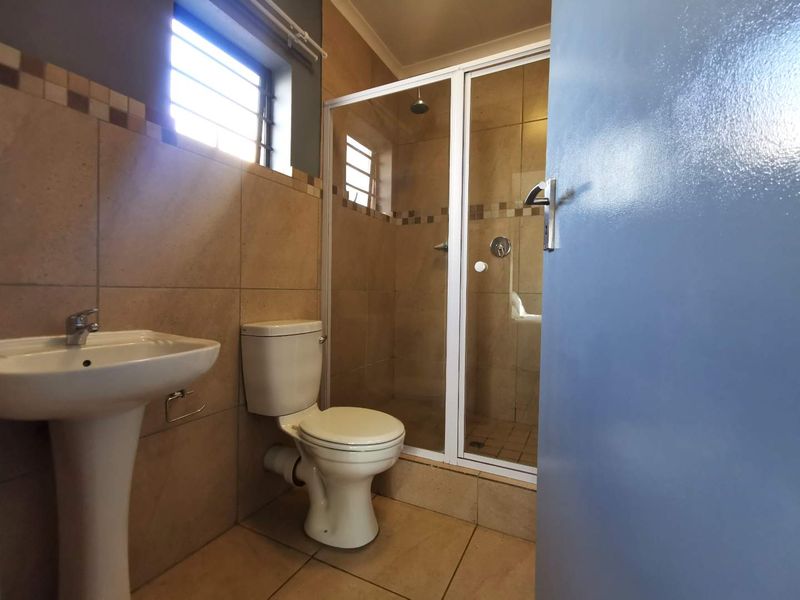 A clean and functional bathroom featuring a pedestal basin, toilet, and a glass-enclosed shower with neutral wall and floor tiling.