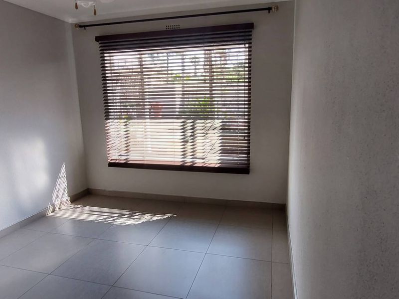 A bright, empty bedroom featuring neutral tiled flooring and fitted venetian blinds, offering a clean and versatile space ready for personalization.