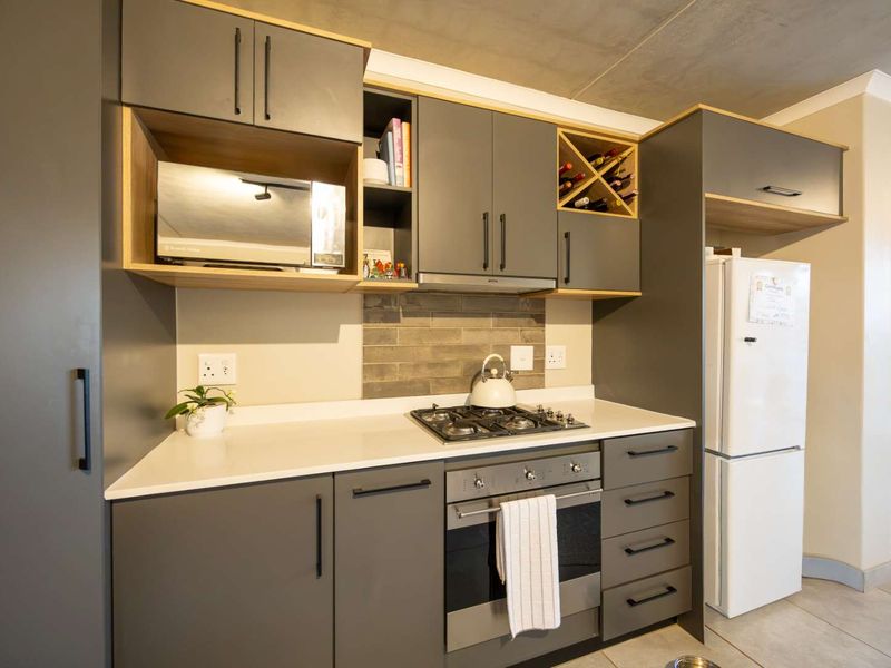 Modern kitchen featuring sleek grey cabinetry, stone countertops, a gas hob, built-in oven, and a dedicated wine rack, offering a contemporary and functional workspace.