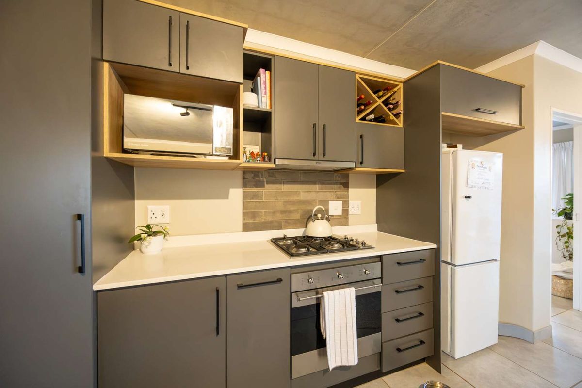 Modern kitchen featuring sleek grey cabinetry, stone countertops, a gas hob, built-in oven, and a dedicated wine rack, offering a contemporary and functional workspace.