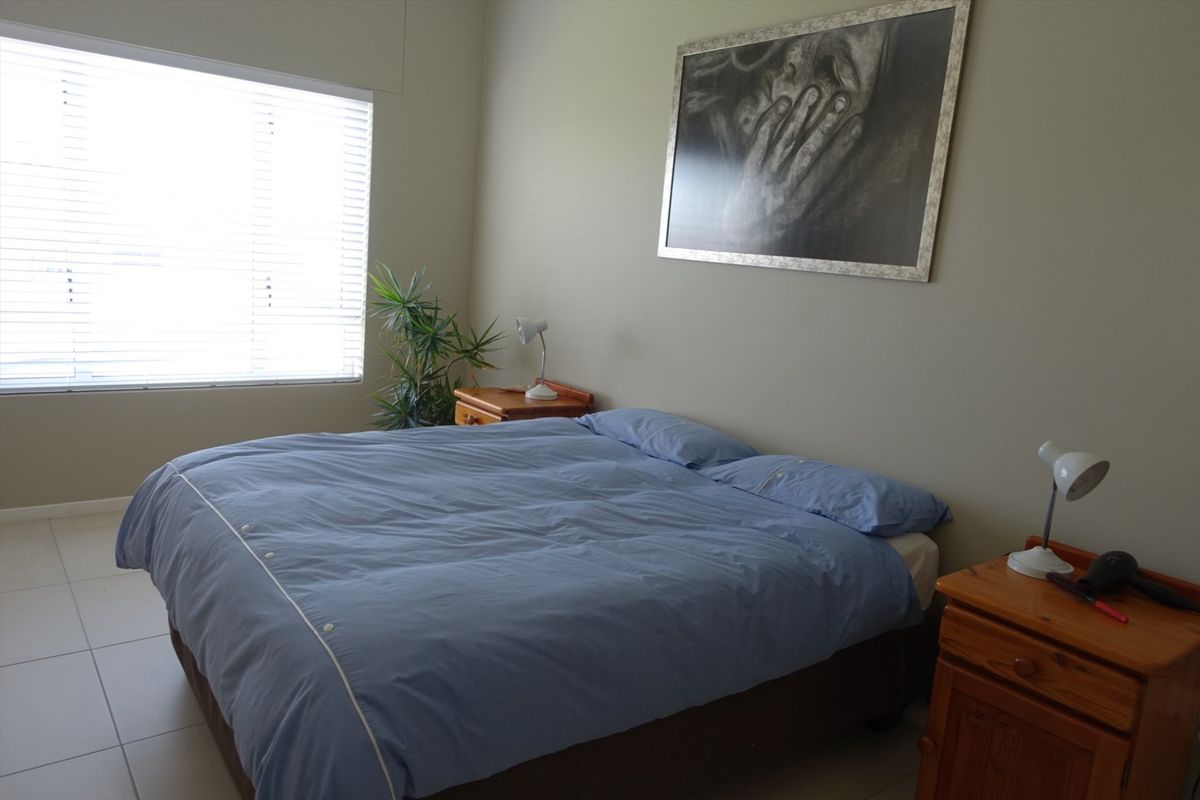 A functional bedroom featuring neutral wall tones, tiled flooring, and a large window fitted with venetian blinds for natural light control.