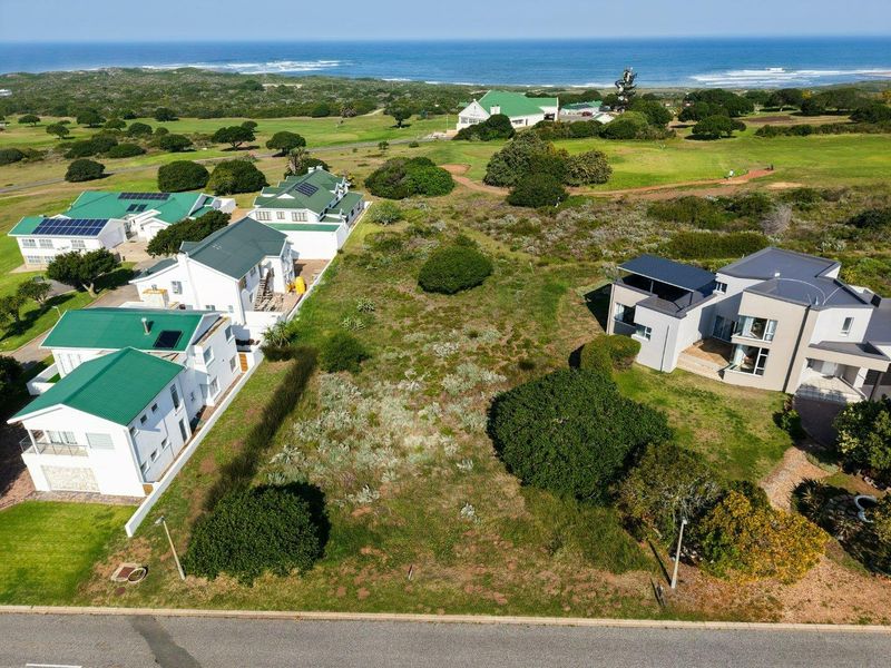 Aerial view of a vacant residential plot situated in a coastal estate, surrounded by established homes and natural vegetation.