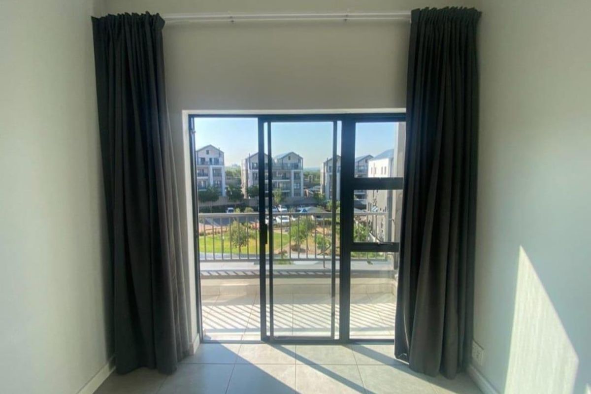 A bright bedroom featuring large sliding glass doors that open onto a private balcony, offering views of the surrounding estate.