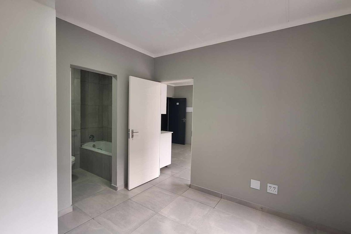 A clean, empty bedroom featuring neutral grey walls, tiled flooring, and direct access to an en-suite bathroom.