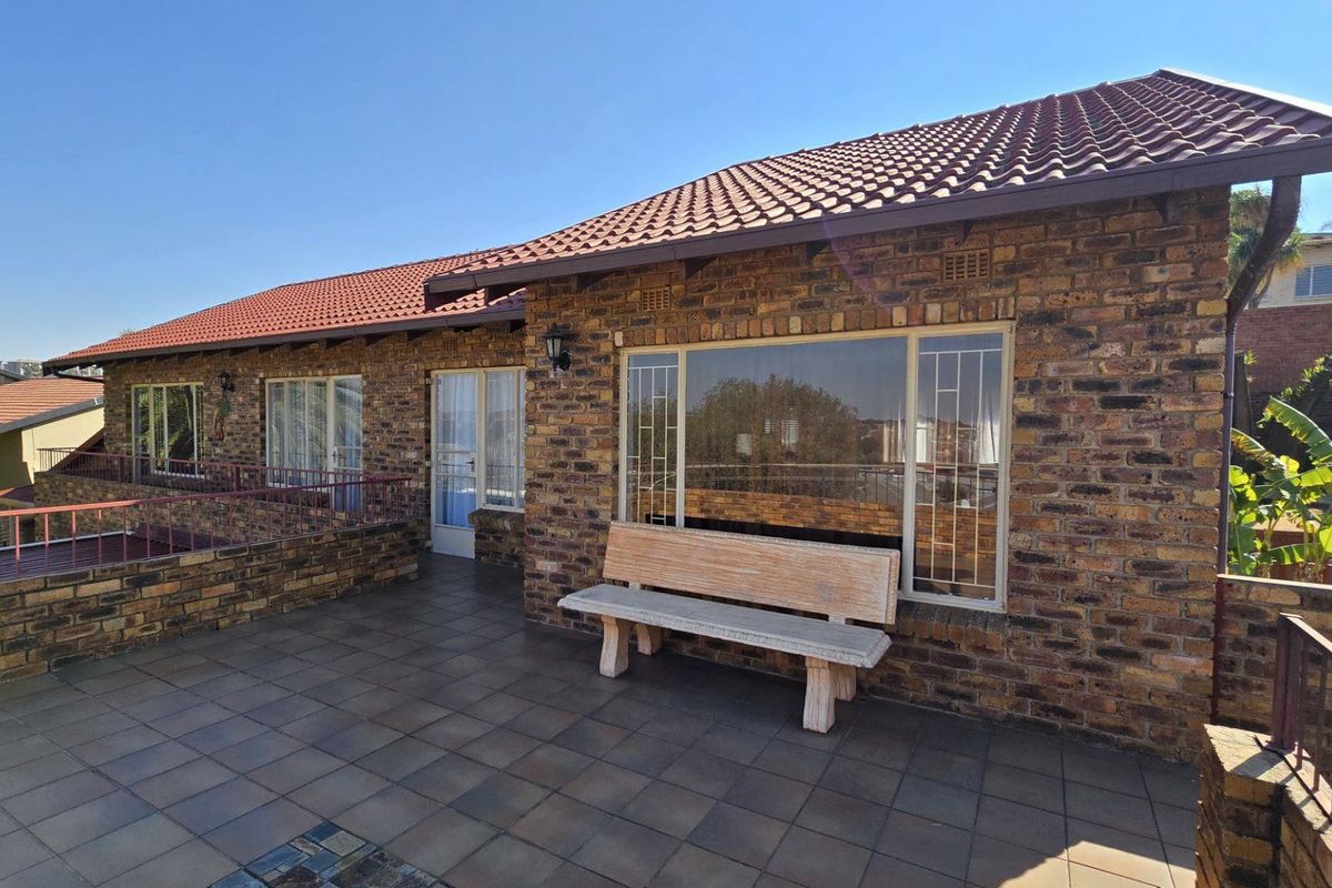 A spacious rear patio area featuring face-brick exterior walls, tiled flooring, and a covered roof structure, providing an ideal space for outdoor relaxation.