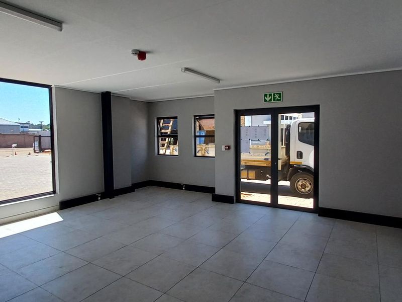 A bright, modern, and empty office space featuring large windows, tiled flooring, and glass panel double doors, suitable for a professional workspace.