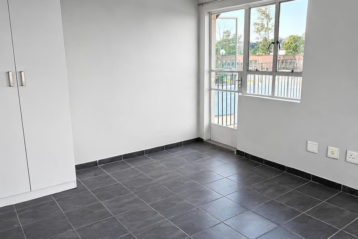 A bright, empty bedroom featuring dark tiled flooring, a built-in wardrobe, and a glass door leading to an outdoor area.