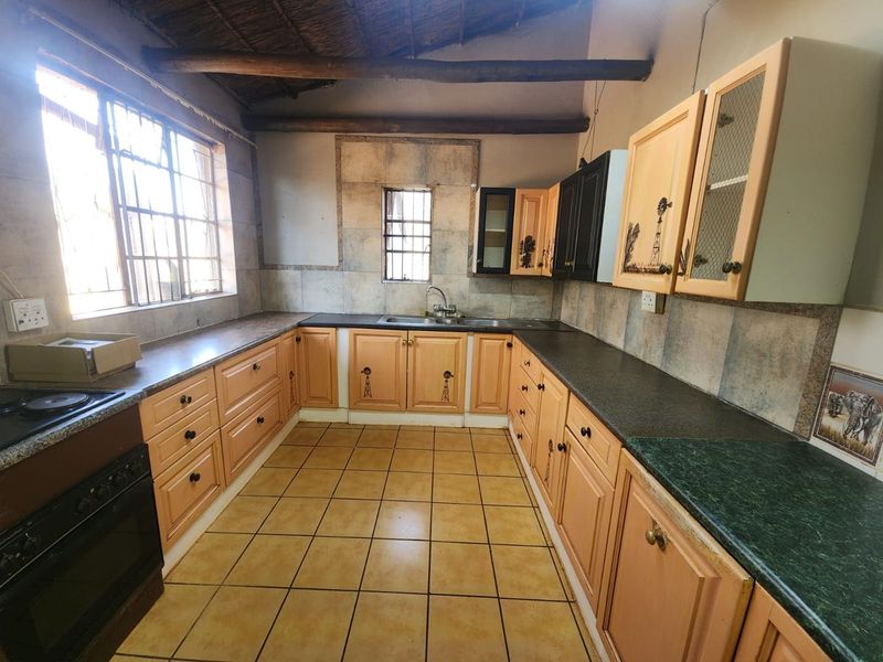 A functional kitchen featuring timber cabinetry, dark countertops, exposed ceiling beams, and tiled flooring, offering a rustic aesthetic with potential for modern updates.