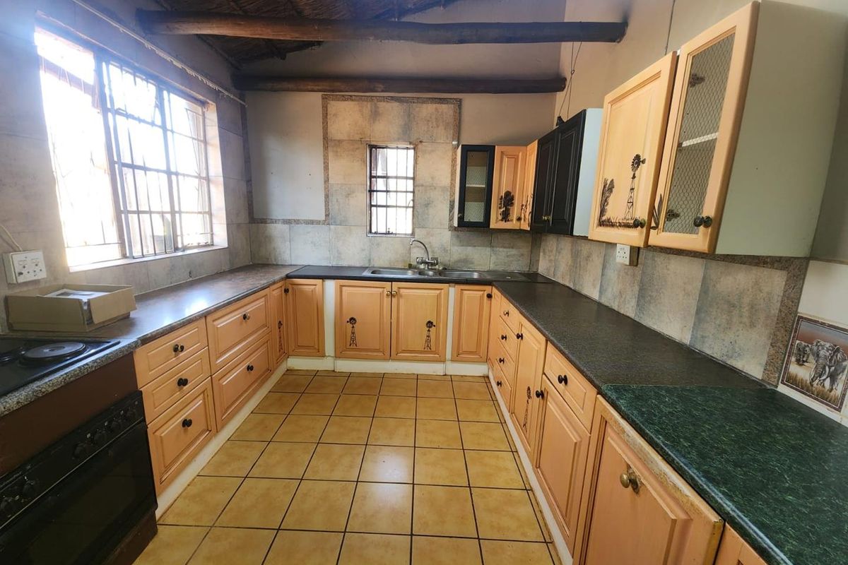 A functional kitchen featuring timber cabinetry, dark countertops, exposed ceiling beams, and tiled flooring, offering a rustic aesthetic with potential for modern updates.