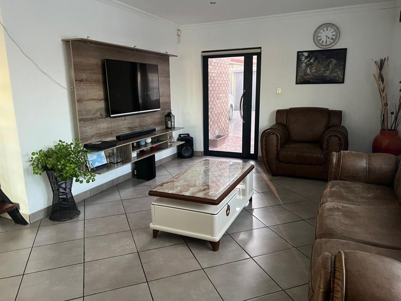 A well-maintained living room featuring tiled flooring and a modern built-in media unit, with direct access to the exterior through a glass panel door.