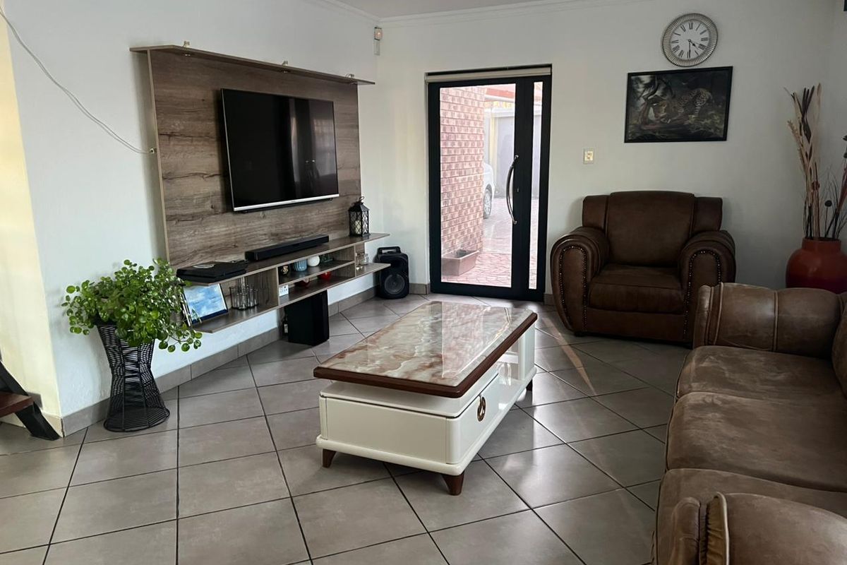 A well-maintained living room featuring tiled flooring and a modern built-in media unit, with direct access to the exterior through a glass panel door.