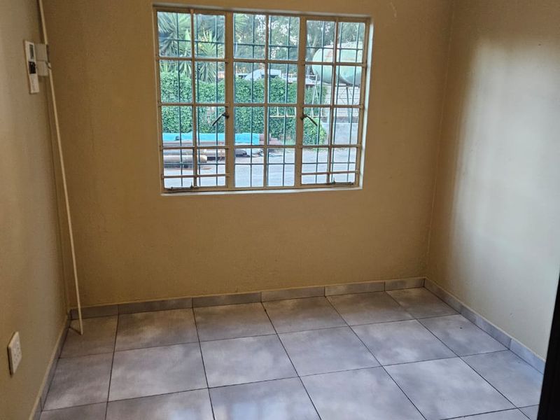 An empty bedroom featuring neutral wall paint, tiled flooring, and a window fitted with security bars.
