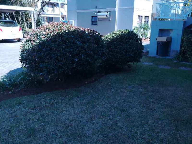Exterior view of the apartment building featuring a landscaped garden area, paved driveway, and covered parking structure.