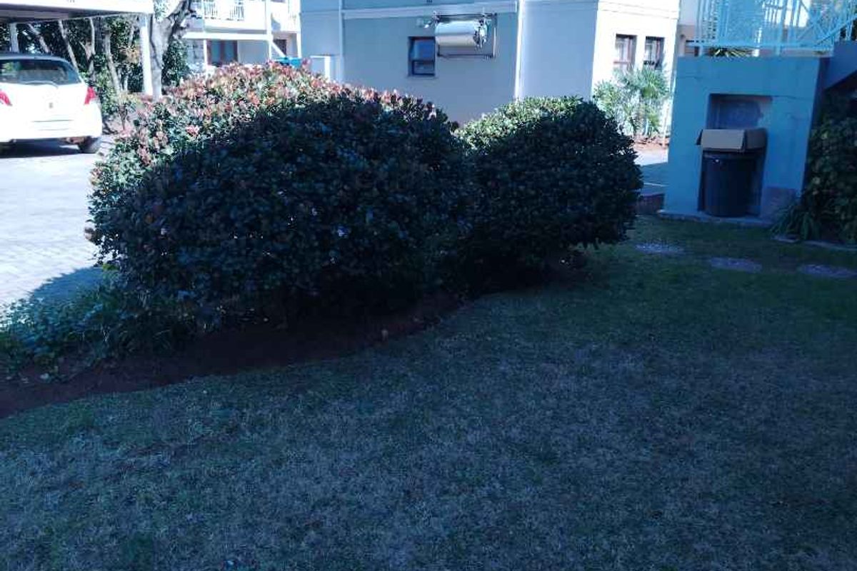Exterior view of the apartment building featuring a landscaped garden area, paved driveway, and covered parking structure.