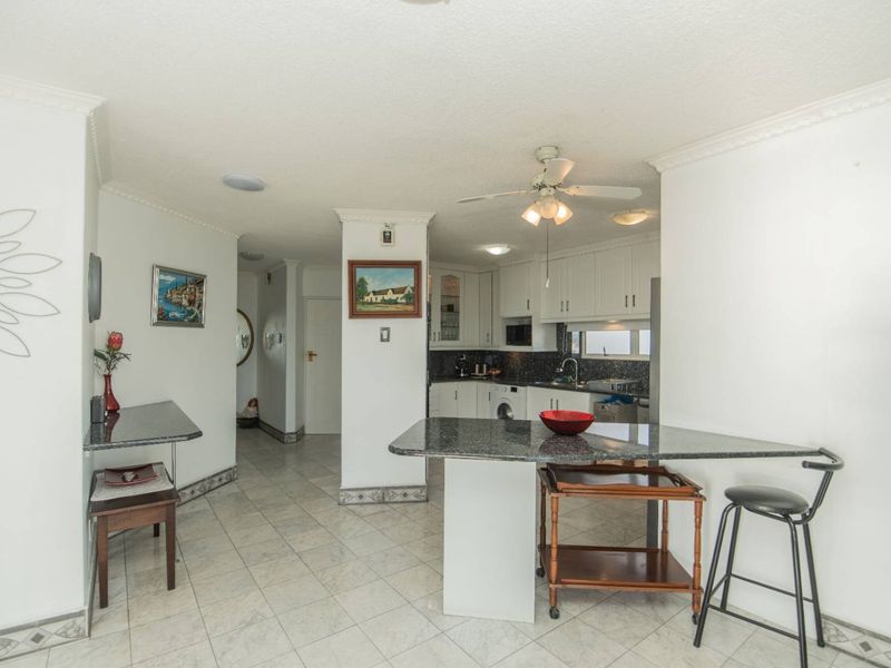 Open plan kitchen and living area featuring white cabinetry, granite countertops, tiled flooring, and a central breakfast bar island.