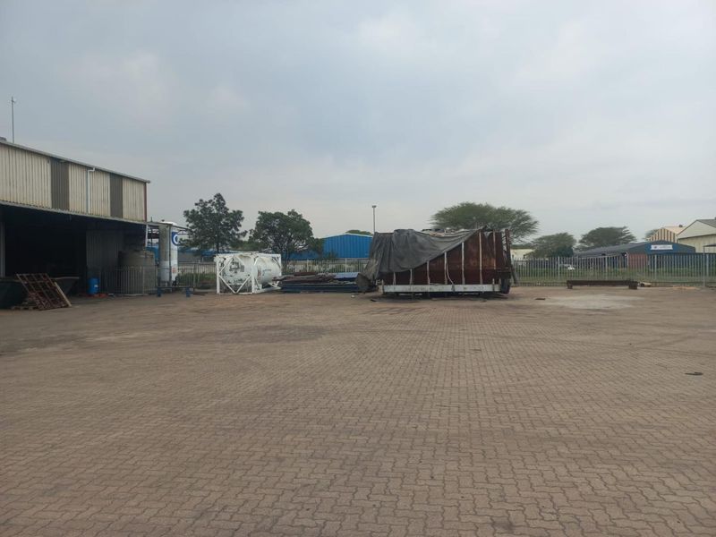 Spacious industrial yard featuring paved ground, perimeter fencing, and access to a large warehouse structure.