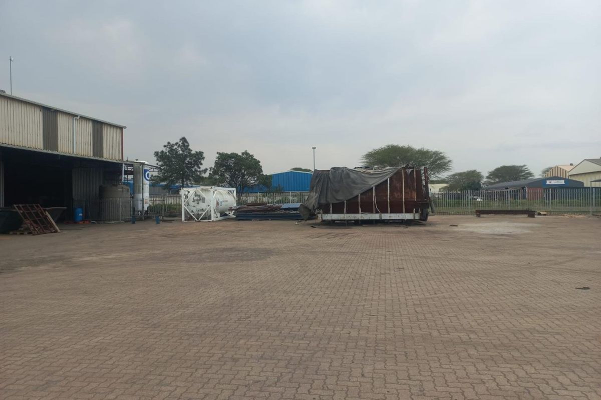 Spacious industrial yard featuring paved ground, perimeter fencing, and access to a large warehouse structure.