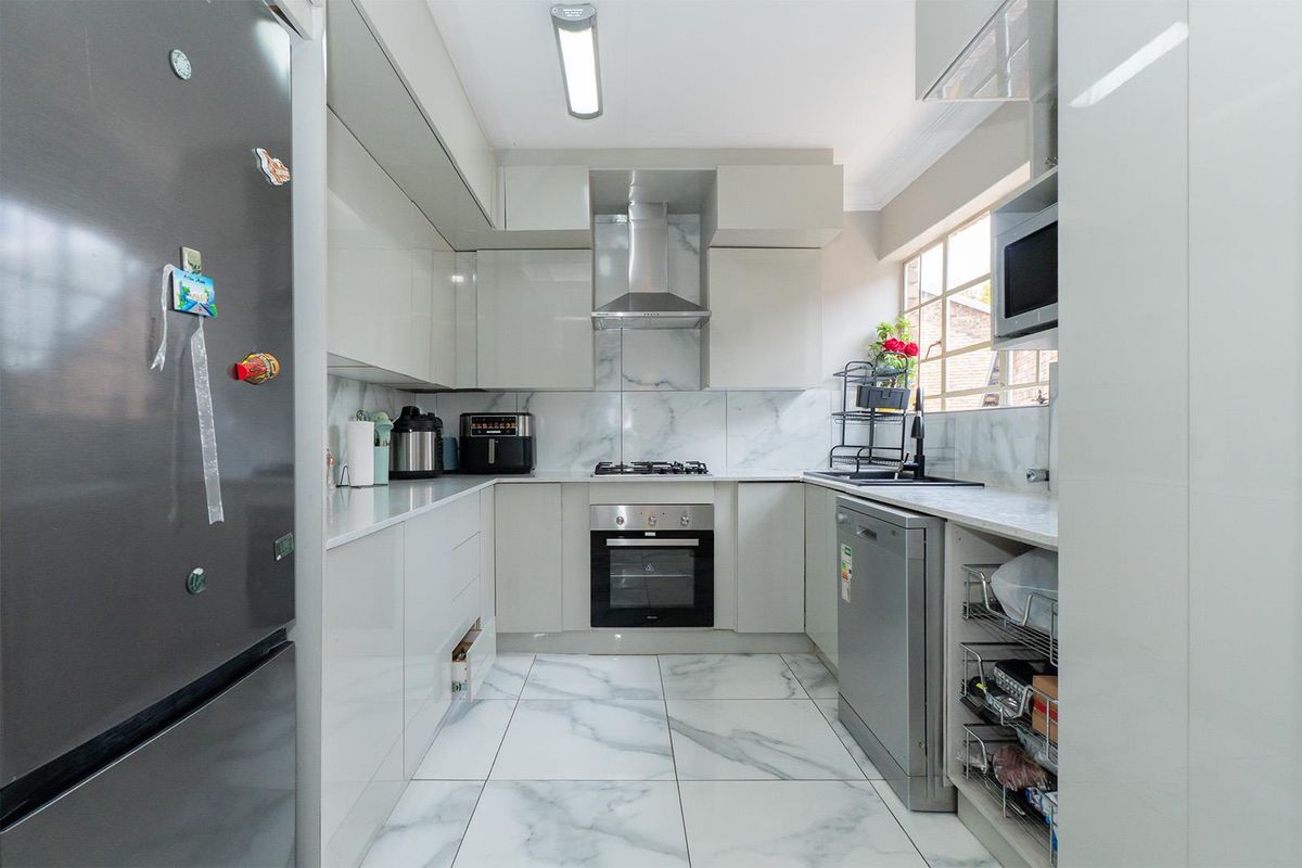 Modern galley-style kitchen featuring high-gloss cabinetry, marble-look tiled flooring, built-in oven, gas hob, extractor fan, and integrated microwave.