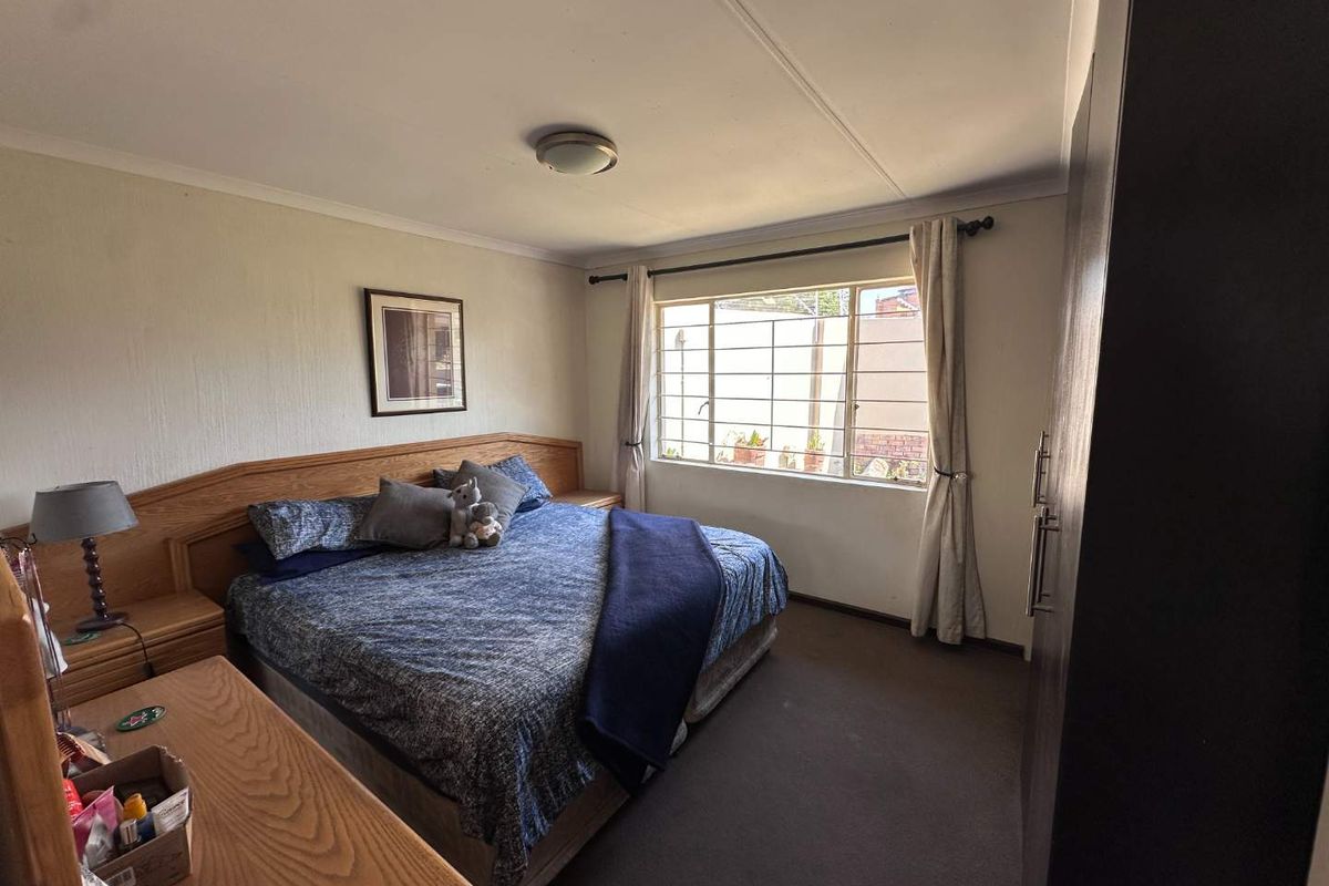 A functional bedroom featuring built-in cupboards, carpeted flooring, and a window fitted with security bars for added peace of mind.