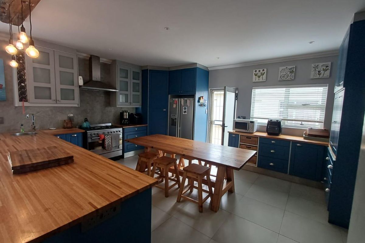 A well-appointed kitchen featuring blue cabinetry, butcher block countertops, a stainless steel gas range with extractor fan, and a central wooden island.