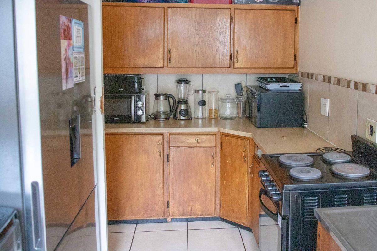A compact kitchen featuring traditional wooden cabinetry, tiled backsplash, and a freestanding electric stove, offering a functional layout with potential for modernization.