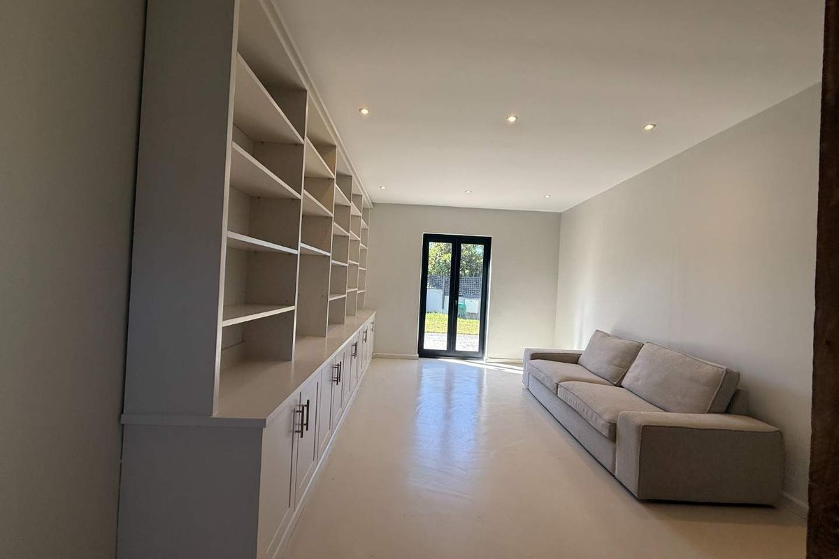 A bright living room featuring extensive built-in cabinetry, recessed lighting, and double glass doors providing access to the outdoor area.