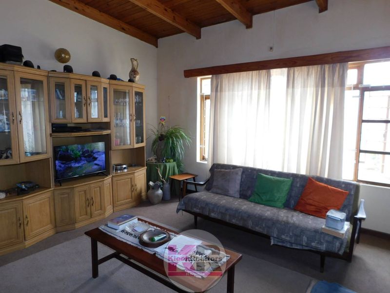 A living room featuring exposed timber ceiling beams, large windows with natural light, and built-in timber cabinetry.