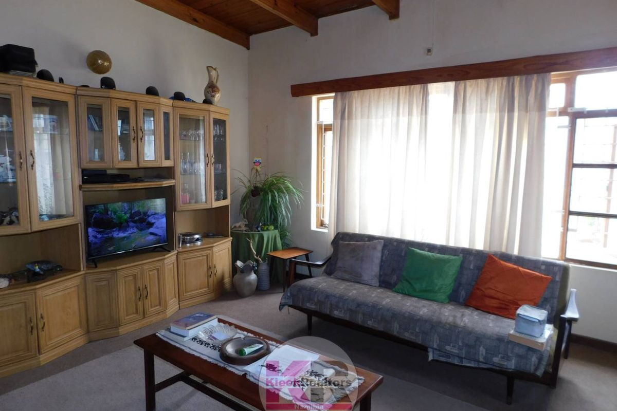 A living room featuring exposed timber ceiling beams, large windows with natural light, and built-in timber cabinetry.