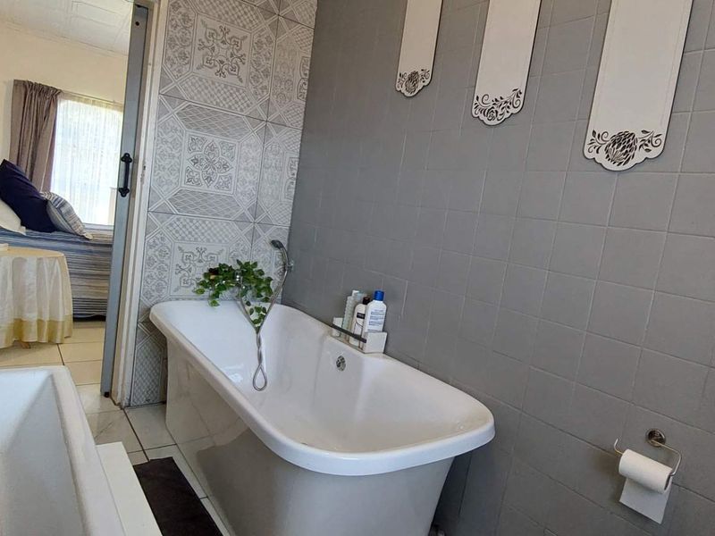 A bathroom featuring a freestanding bathtub with grey tiled walls and patterned accent tiling, providing a functional space with direct access to the bedroom.