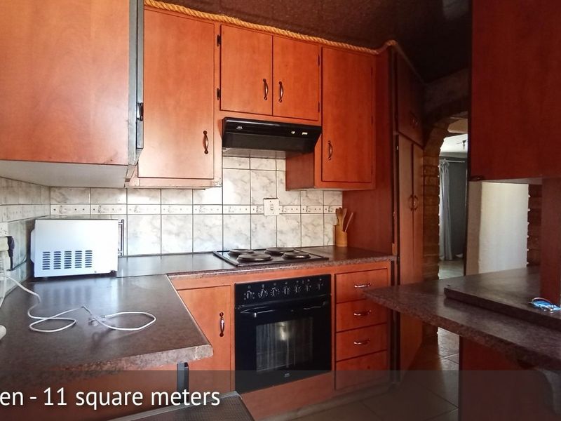 A compact kitchen featuring dated wooden cabinetry, laminate countertops, a built-in oven with hob, and a tiled backsplash.