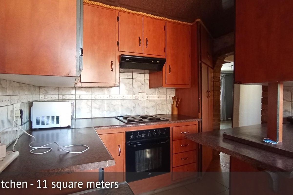 A compact kitchen featuring dated wooden cabinetry, laminate countertops, a built-in oven with hob, and a tiled backsplash.