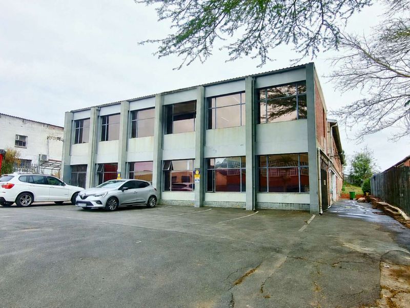 Front exterior view of a two-story industrial building featuring a concrete facade, large windows, and an adjacent asphalt parking area.