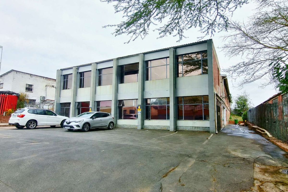 Front exterior view of a two-story industrial building featuring a concrete facade, large windows, and an adjacent asphalt parking area.