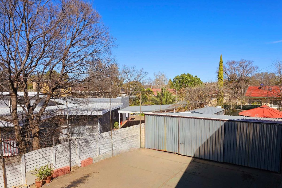 An elevated view of the rear property area featuring a paved courtyard, metal storage structures, and perimeter fencing.