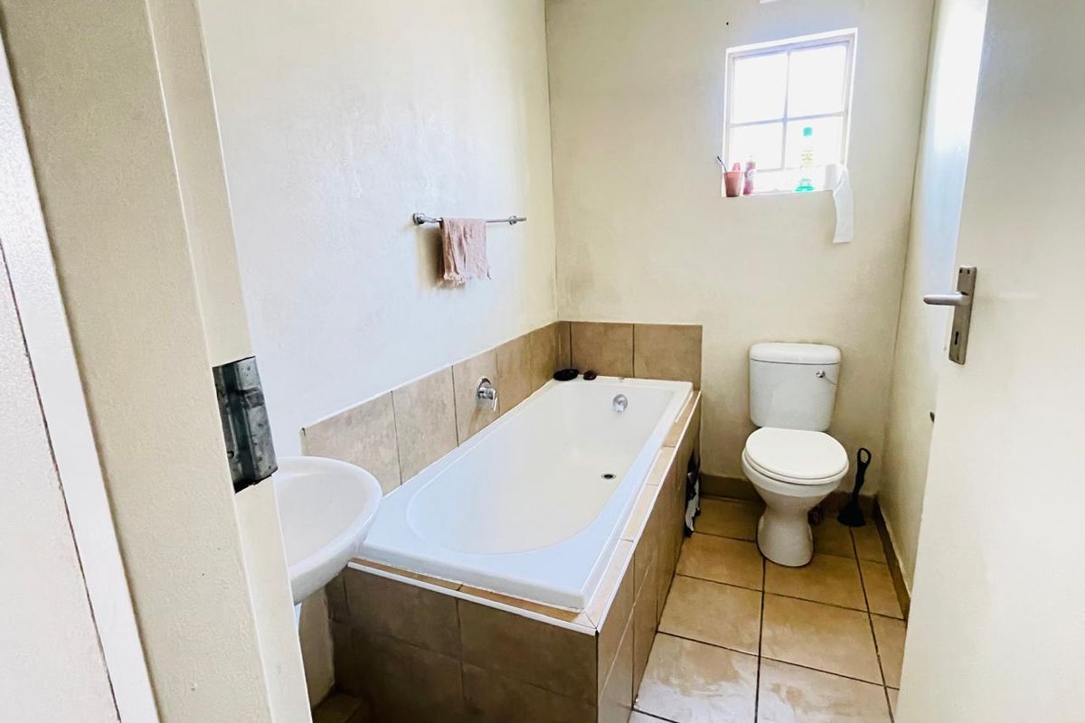 A functional bathroom featuring a built-in bathtub with tiled surround, a pedestal basin, and a standard toilet.
