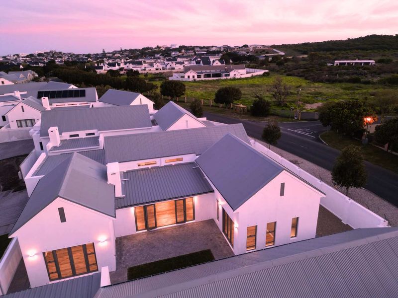 Aerial view of a modern residential property featuring a white facade, corrugated metal roofing, solar panels, and a paved courtyard at dusk.