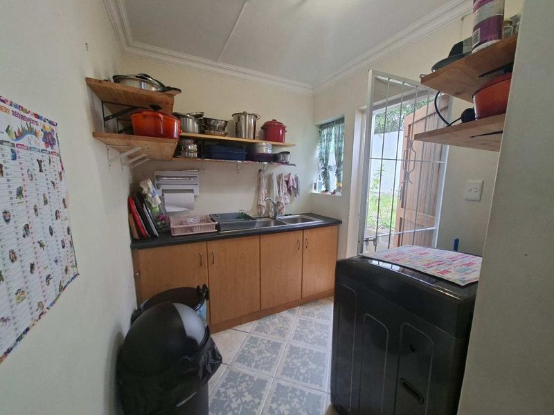 Functional laundry area featuring laminate cabinetry, double stainless steel sink, tiled flooring, and direct access to the rear garden via a security gate.