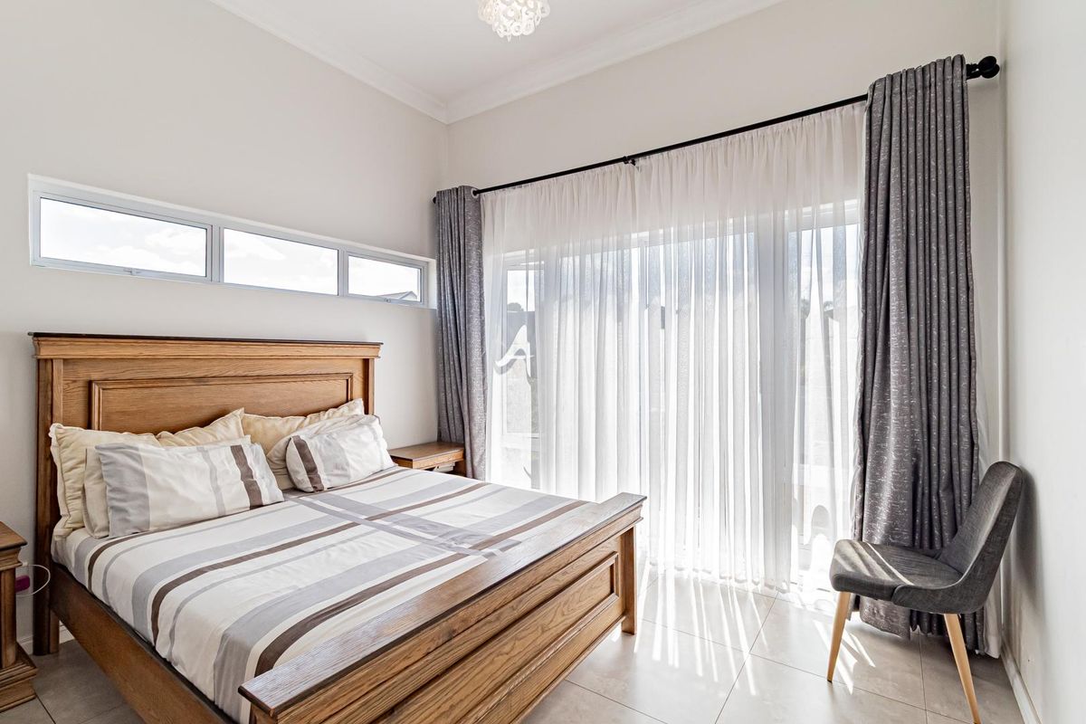 A bright and spacious bedroom featuring large sliding glass doors with sheer curtains, tiled flooring, and high ceilings with decorative cornice.