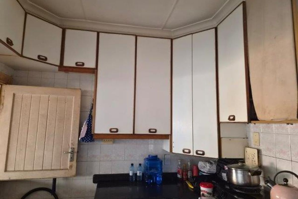 A dated kitchen featuring white laminate cabinetry, dark stone countertops, and a tiled backsplash, offering potential for a modern renovation.