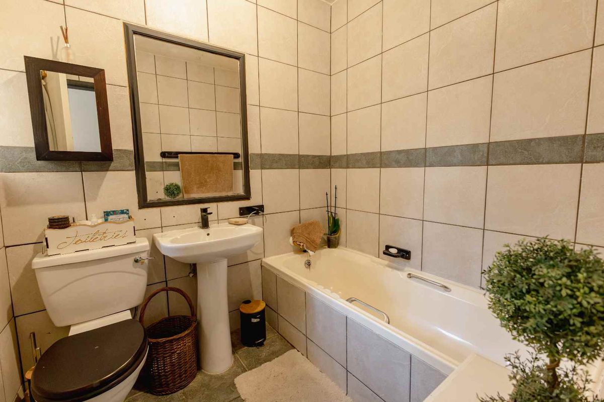 A functional bathroom featuring a pedestal basin, bathtub, and neutral wall tiling, offering a clean and practical space.