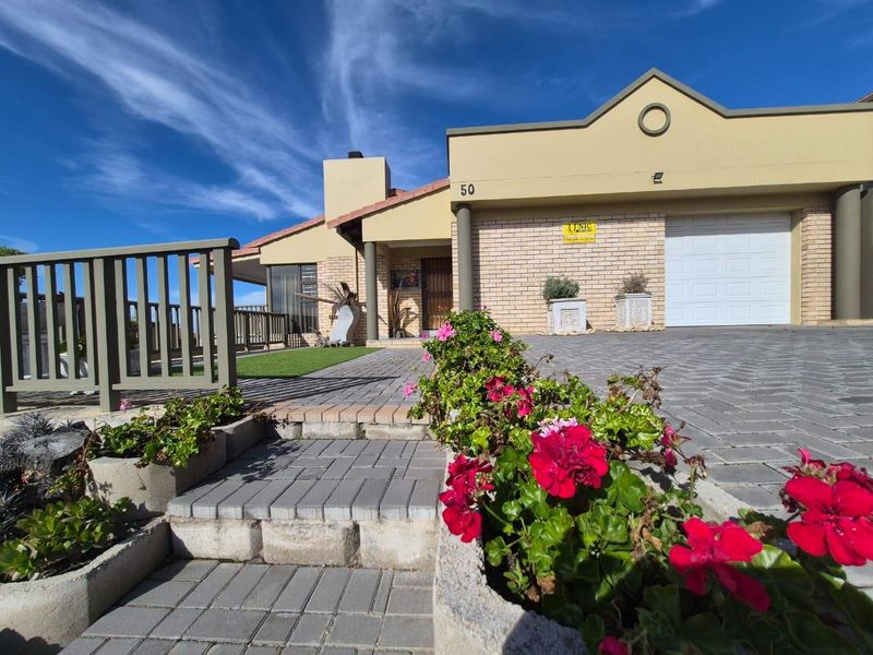 Front view of a single-story house featuring a paved driveway, garage, and landscaped retaining wall with a brick facade.